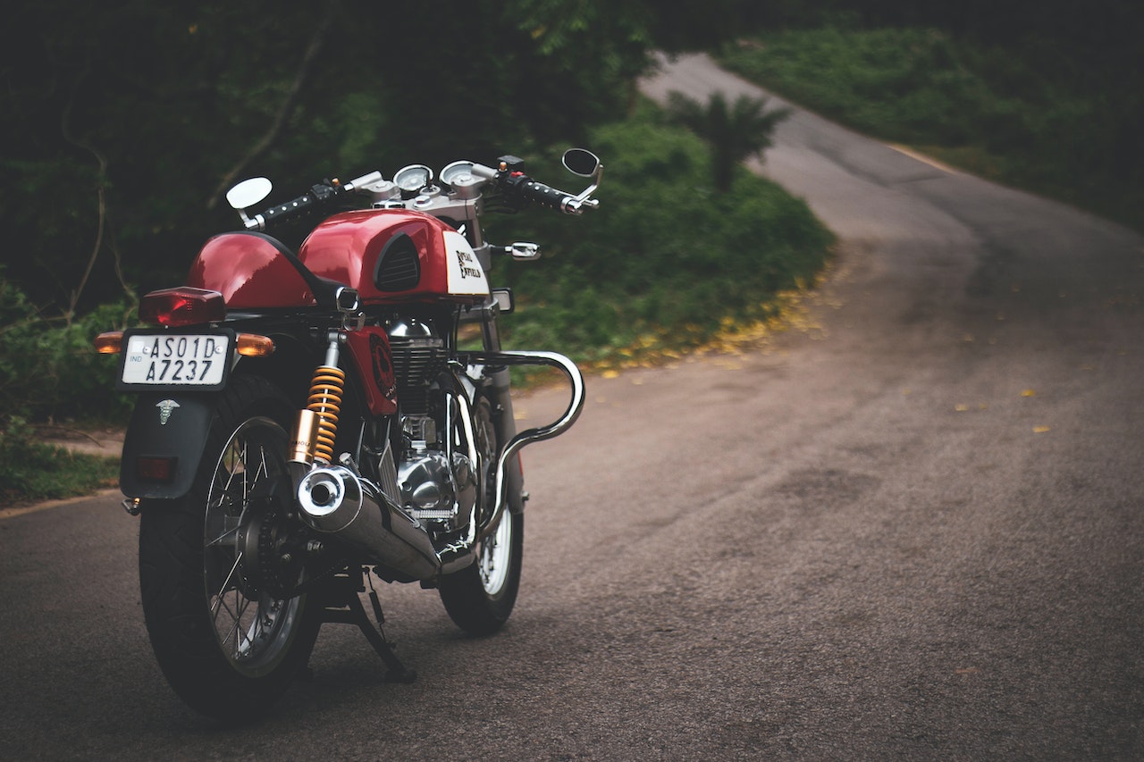 Classic red motorcycle parked on a winding road surrounded by lush greenery.