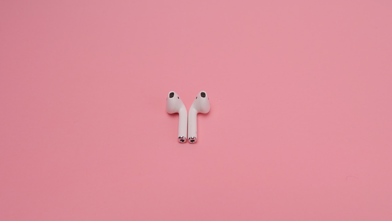 Pair of white wireless earbuds on a pink background, resembling Apple's AirPods.