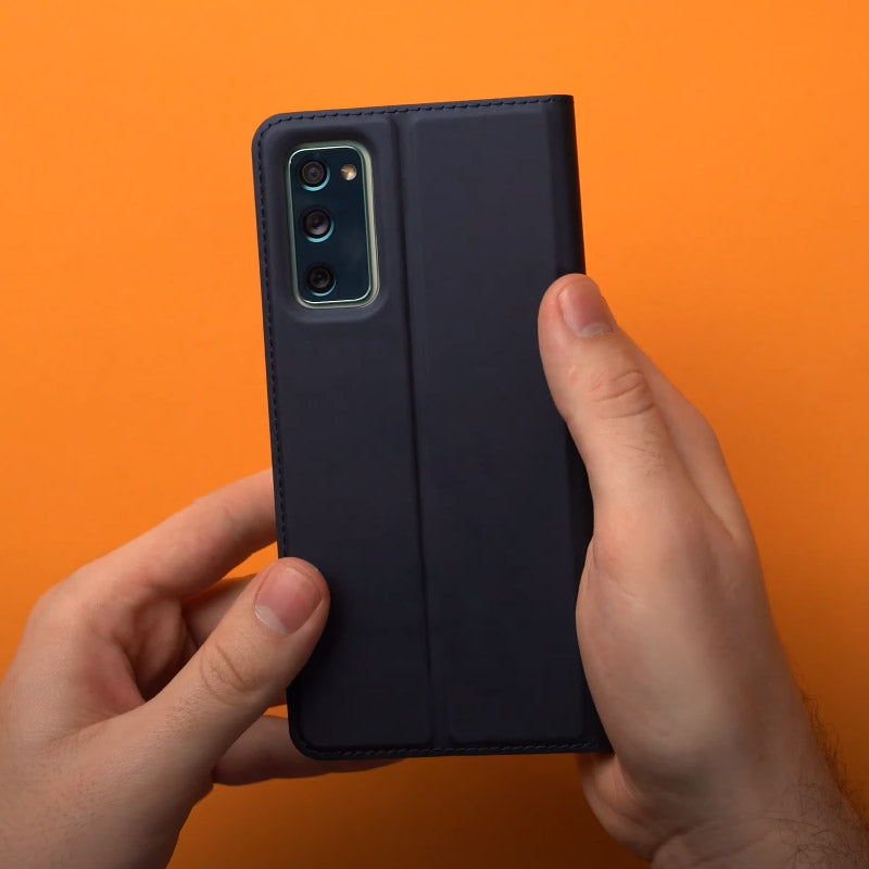 Person holding Samsung Galaxy S20 FE with protective case against orange background.