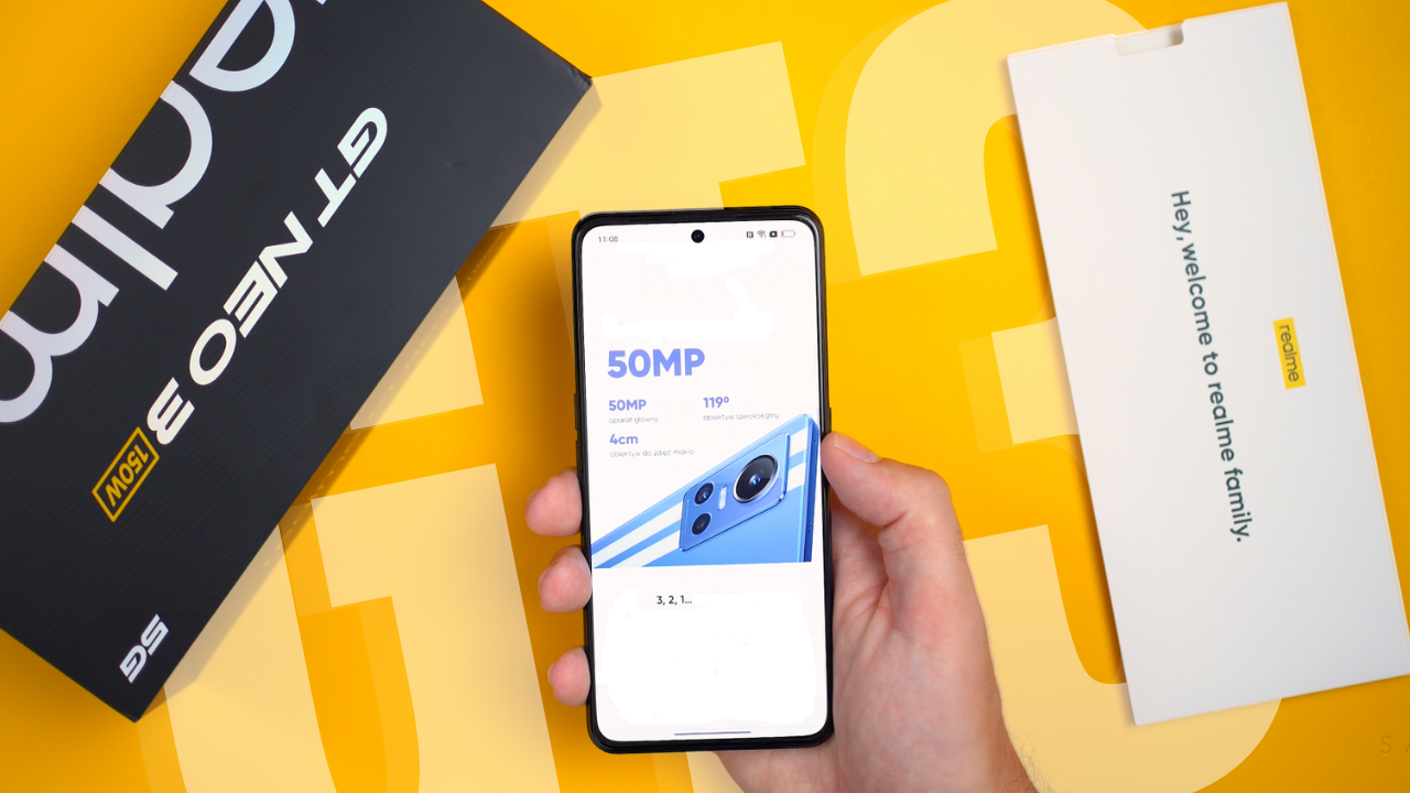 Hand holding Realme GT Neo 3 smartphone with 50MP camera feature displayed on screen, alongside box and packaging on yellow background.