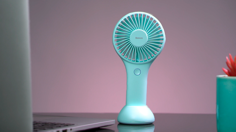 Baseus Bingo portable USB fan in blue on a desk with a laptop and plant, designed for hand and desktop use.