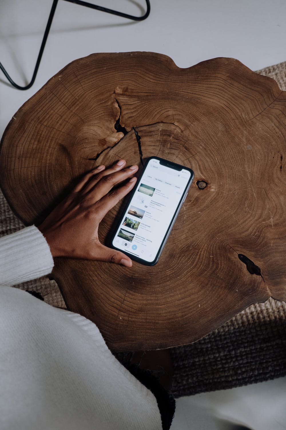 Hand touching iPhone 13 Pro Max placed on a wooden table, displaying search results.