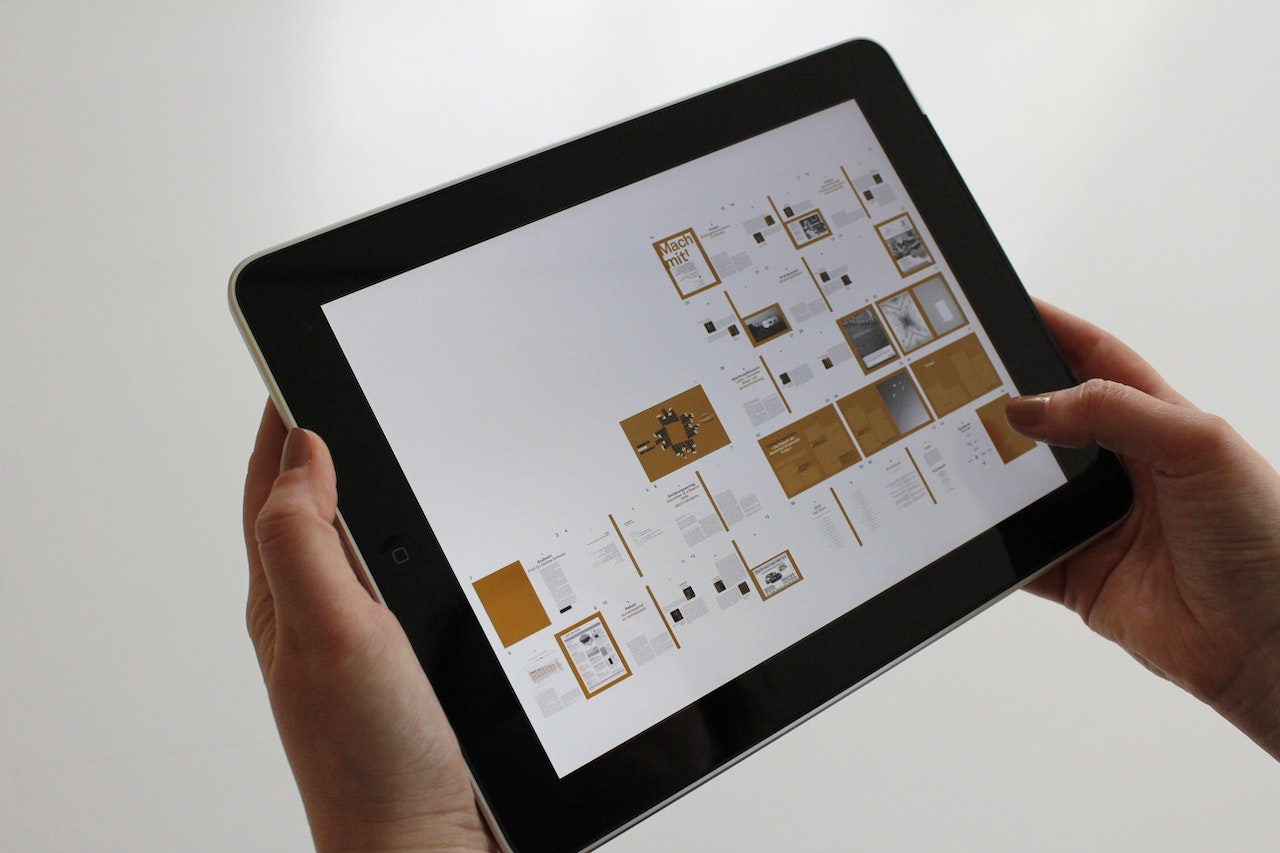 Person holding a tablet displaying a grid of apps on a light background.