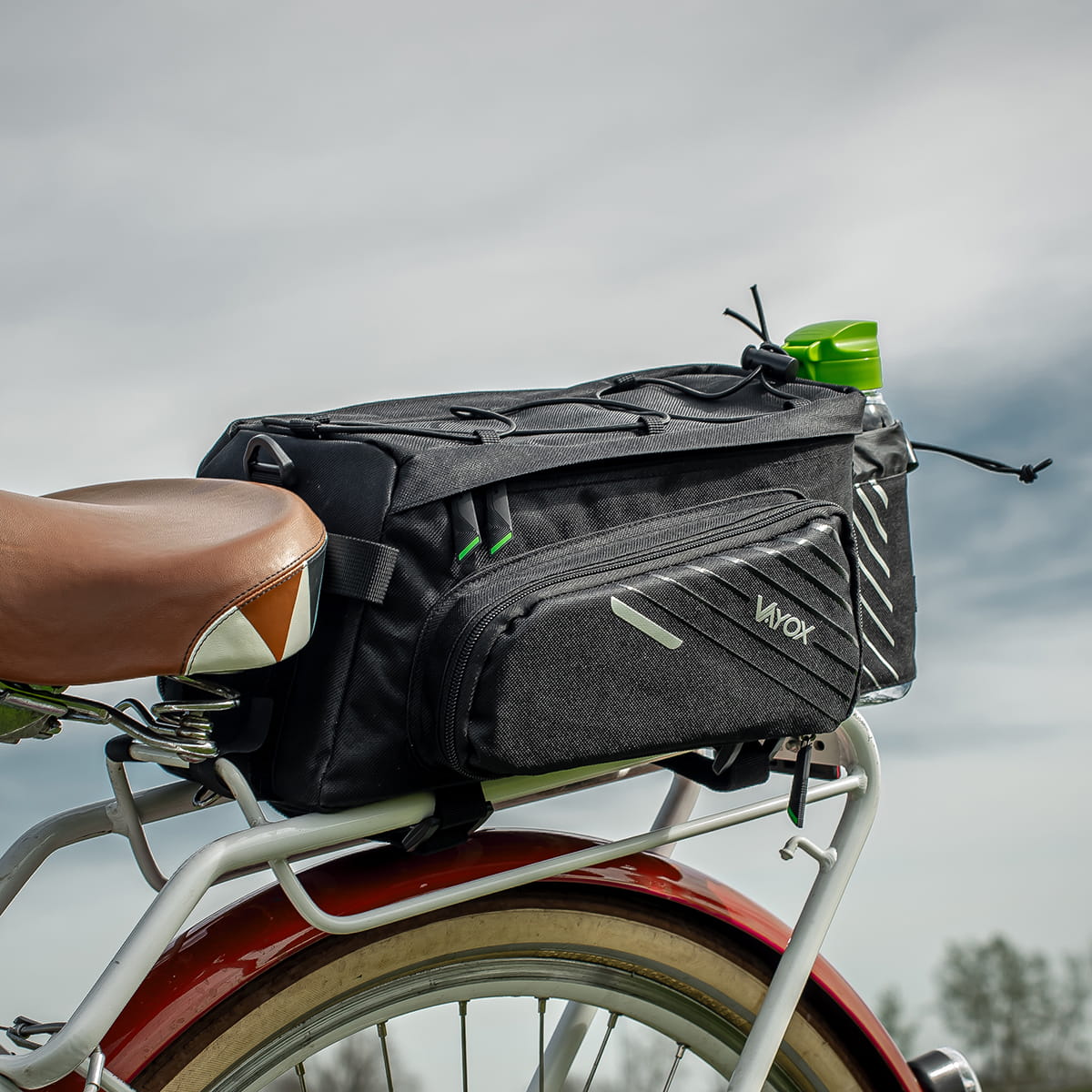 Fahrradtasche Vayox VA0171 12L in Schwarz auf einem Gepäckträger montiert, mit seitlichem Reißverschluss und grünem Trinkflaschenhalter.