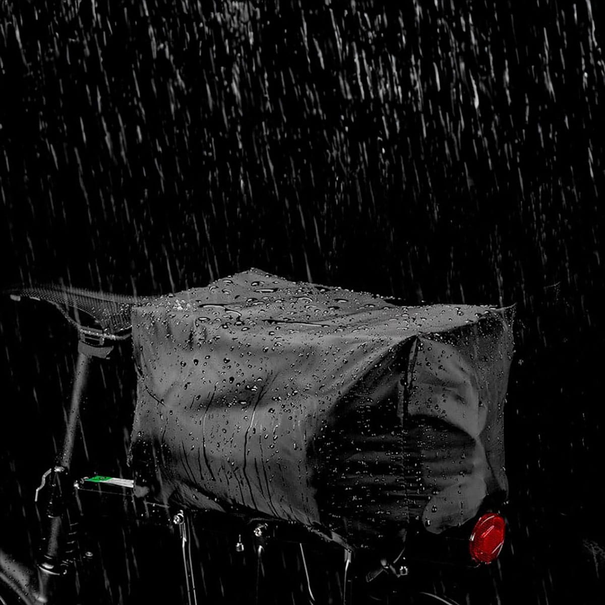 Black Vayox VA0171 bike bag on rack, under heavy rain, showcasing water-resistant durability and adjustable 12L capacity.