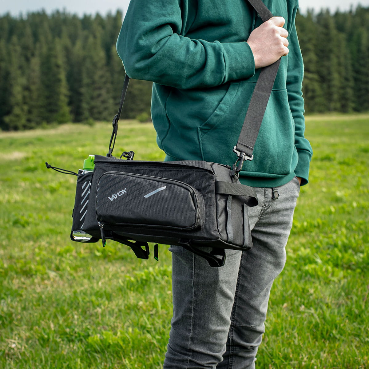 Person carrying Vayox VA0171 black bike cargo bag as shoulder bag with adjustable capacity, nylon and polyester material, outdoors.