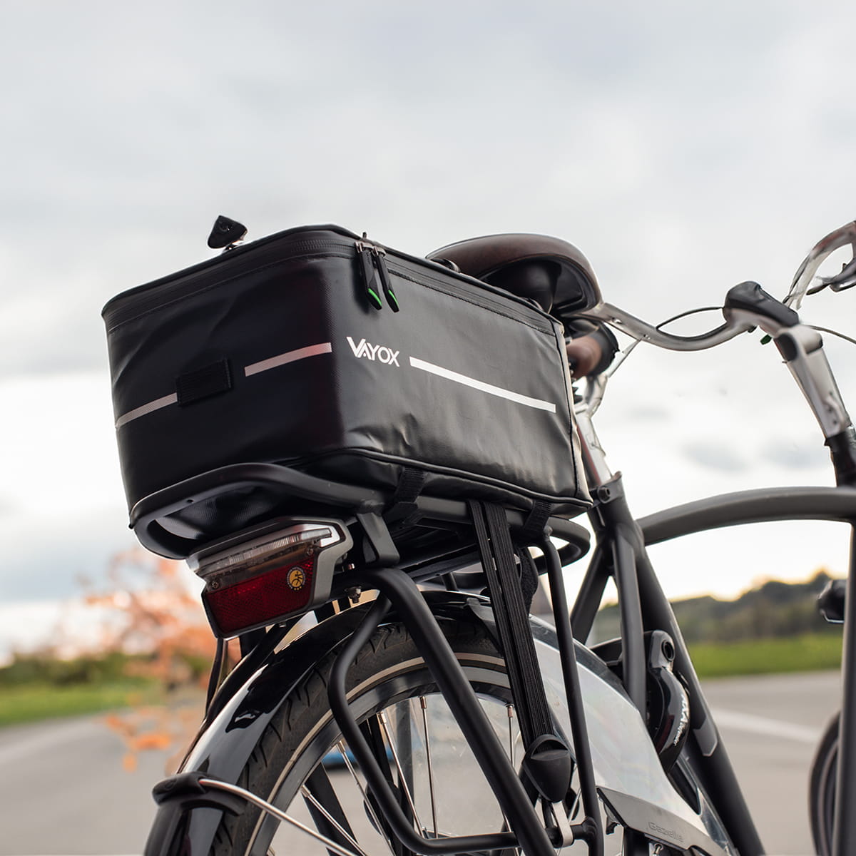 Schwarze Vayox VA0166 8L Fahrradtasche auf Gepäckträger montiert, ideal für Radfahrer, mit Klettverschlüssen, auf Landstraße.