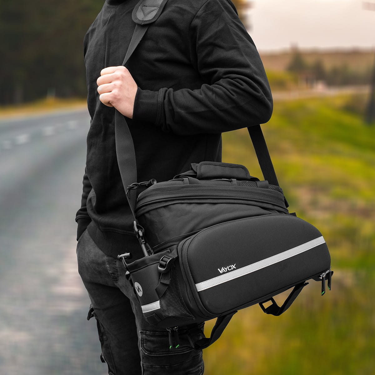Man carrying Vayox VA0346 black 35L bike pannier bag on shoulder by the road