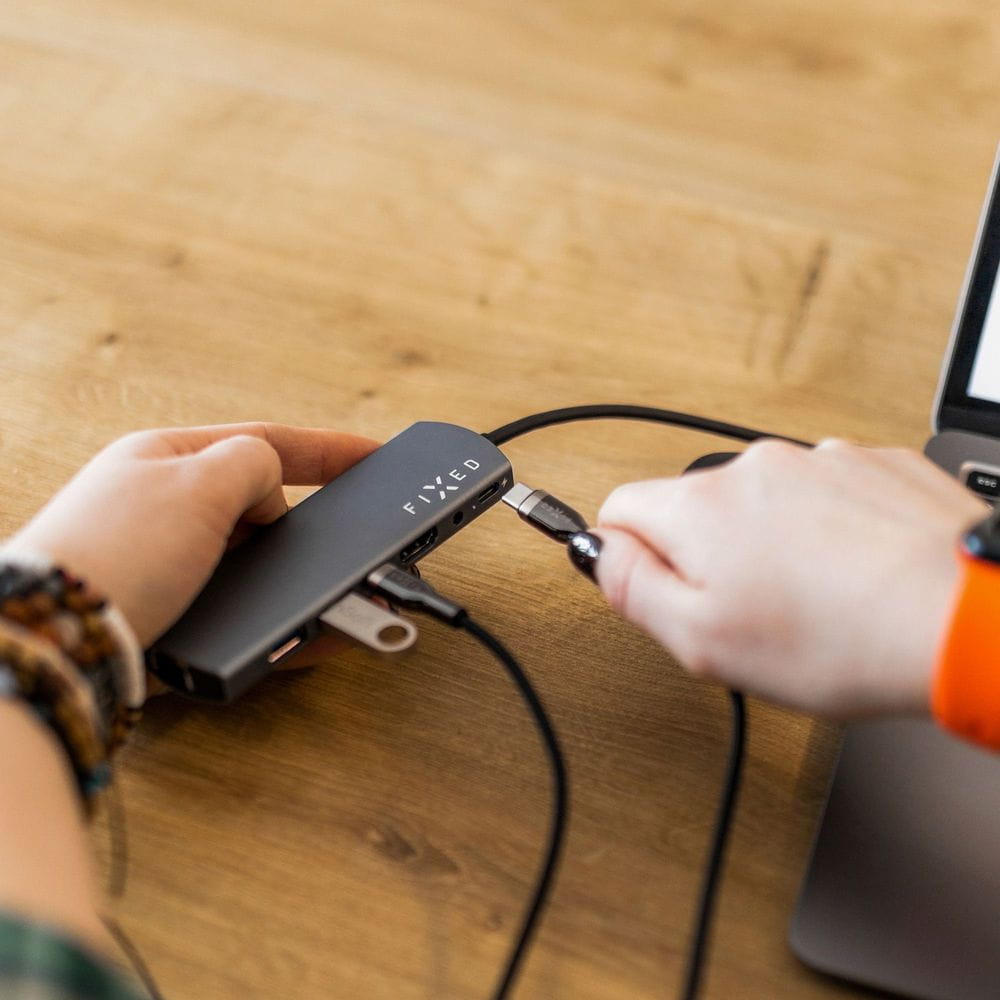 Person verbindet Laptop mit FIXED USB-C Hub auf Holztisch.