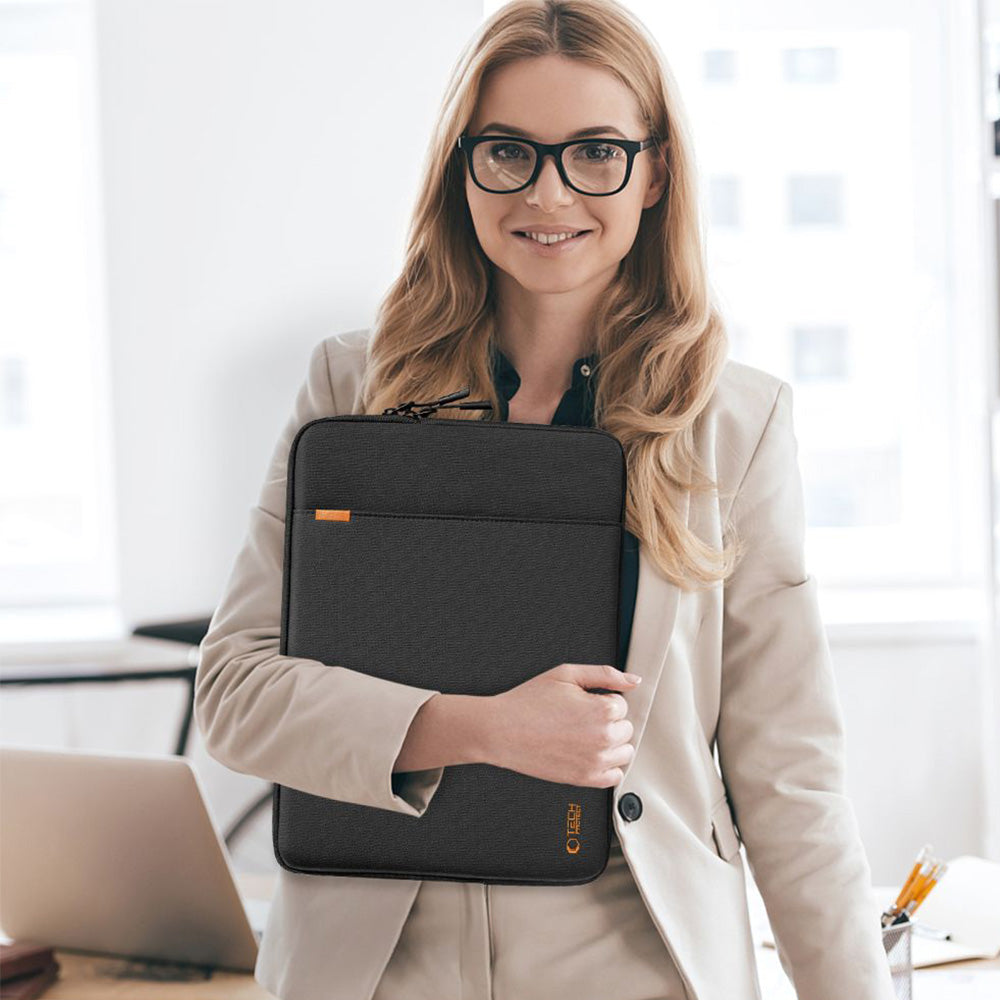 Professionelle Frau in Anzug hält schwarze Laptop-Tasche für 15-16 Zoll mit einem Lächeln in modernem Büro.